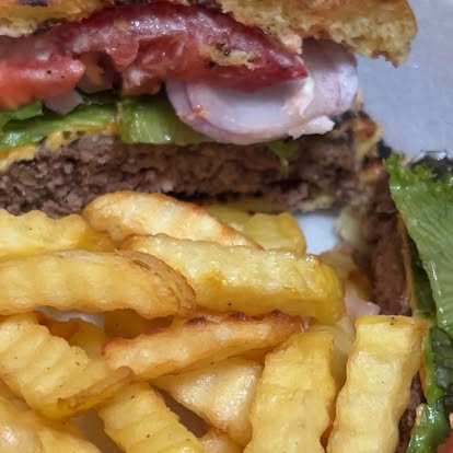 A burger with a bite taken from the top bun, served with fries.