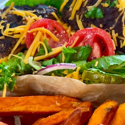 A loaded burger with shredded cheese and tomato, with sweet potato fries.
