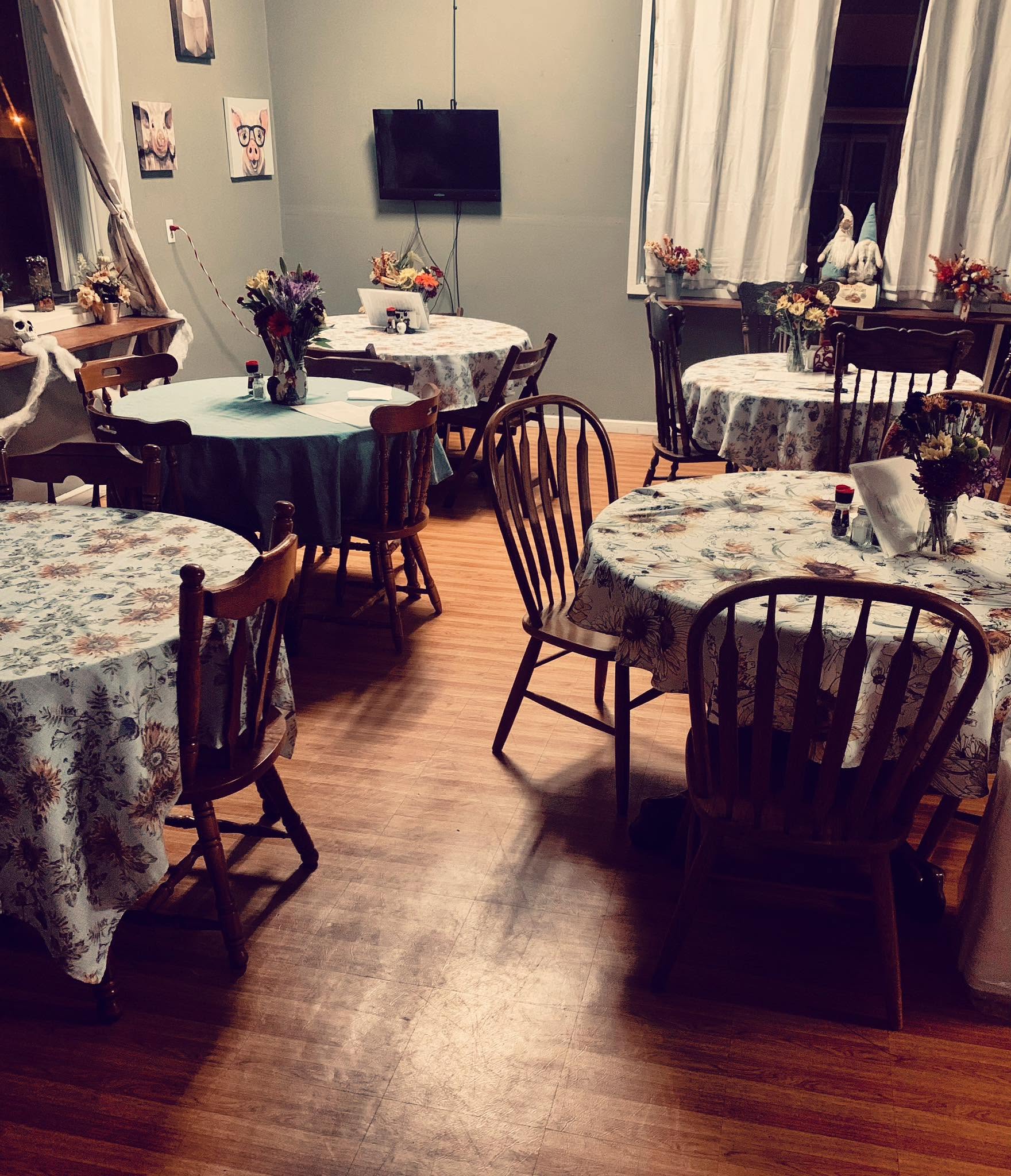 The dining room: set tables with floral cloths and wooden chairs.