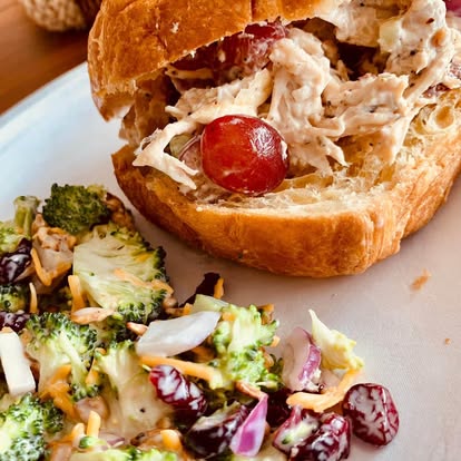 A chicken salad croissant sandwich with a side salad.