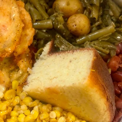 A fried chicken plate with cornbread, greens and corn.