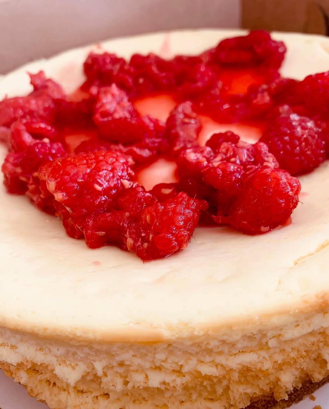 A slice of New York-style cheesecake topped with fresh raspberries.
