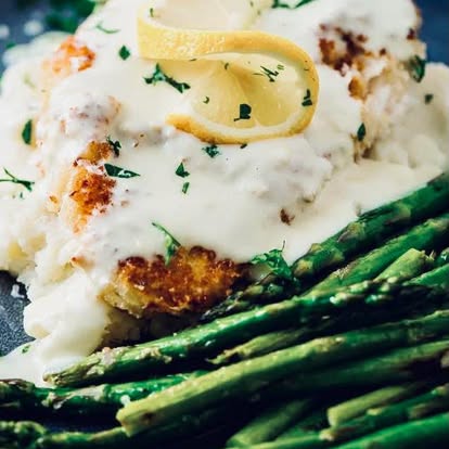 A fish fillet with lemon over asparagus and mashed potatoes.
